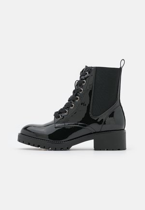 Bottine noire en cuir verni à lacets, avec panneaux latéraux élastiques, languette de tirage, talon épais et semelle robuste.