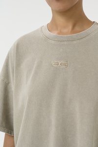 Oversized beige cotton t-shirt with a round neckline and embroidered logo on the chest. Soft texture with a subtle faded appearance.