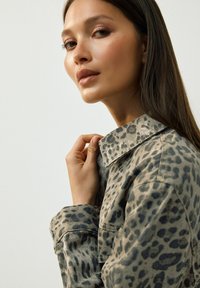Leopardmönstrad skjorta med krage, långa ärmar och en strukturerad tyg i nyanser av beige och mörkbrun.