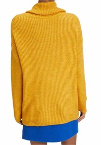 Senapsgul oversized tröja med ribbad textur, hög krage och sänkt axel. Matchad med en blå minikjol i mitten av lårlängd.