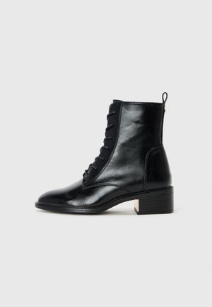 Black leather ankle boot with a smooth finish, lace-up design, rounded toe, and a low block heel featuring a metallic accent on the heel.
