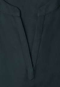Gros plan sur un tissu sombre avec une encoche en forme de V et une double couture visible le long des bords.
