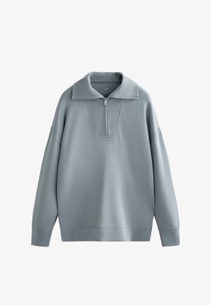 Pullover grigio chiaro con collo a mezza zip, maniche ampie e un pannello alare strutturato. Realizzato in un tessuto morbido e liscio con vestibilità rilassata.