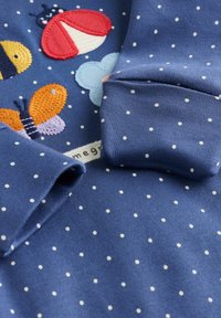 Blå bomullströja med vita prickar och broderade insekter (bi, nyckelpiga, fjäril) med texturerad sömnad och vikta ärmslut.