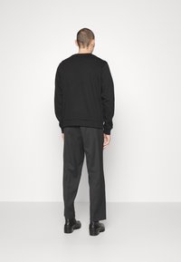 Černá mikina s kulatým výstřihem a žebrovaným lemem, doplněná tmavě šedými kalhotami. Boty jsou černé s nízkou, masivní podrážkou.