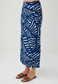 Gonna maxi blu navy con motivi a foglia bianchi. Realizzata in tessuto testurizzato, presenta una vita adattata e una silhouette dritta. Sandali piatti marroni.