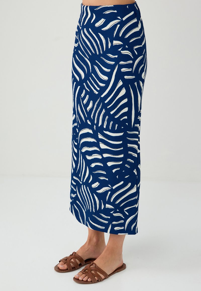 Gonna maxi blu navy con motivi a foglia bianchi. Realizzata in tessuto testurizzato, presenta una vita adattata e una silhouette dritta. Sandali piatti marroni.