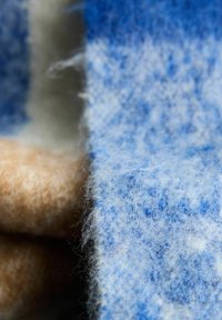 Felt fabric in blue and beige, featuring a soft, fuzzy texture with a subtle pattern. Edges are irregular and frayed.