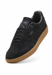 Svart mockaskinnsneaker med texturerad ovandel, rund tå och gummisula. Har snörning och subtila varumärkesakcenter.