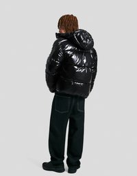 Black, glossy puffer jacket with a hood, featuring quilted sections; paired with dark denim pants and black sneakers.