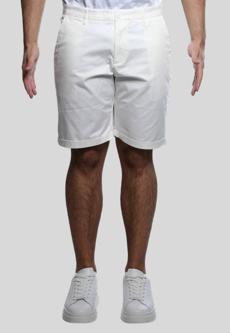 Bermuda bianca in cotone con fronte piatto, tasche a fessura e risvolti, abbinate a scarpe da ginnastica bianche. Design semplice e pulito.