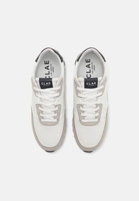 Baskets véganes blanches avec des détails en mesh et en daim, présentant des accents gris, un talon noir et des lacets blancs. Logo sur la languette.