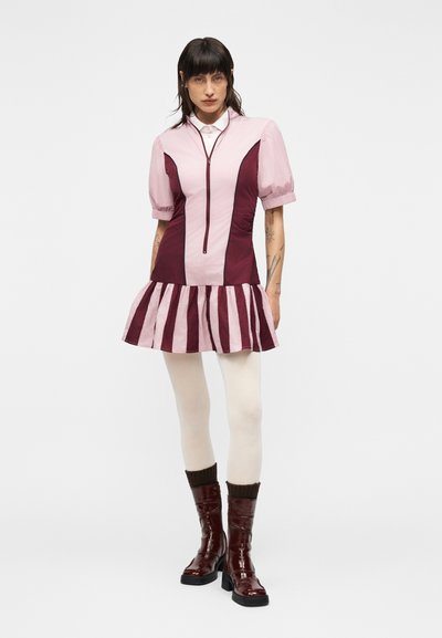 Μίνι φόρεμα με μπλοκ χρωμάτων σε ροζ και βουργουνδί, με φουσκωτά μανίκια, φερμουάρ κλεισίματος και ριγέ λεπτομέρειες στη φούστα. Καφέ μποτάκια στρατού.