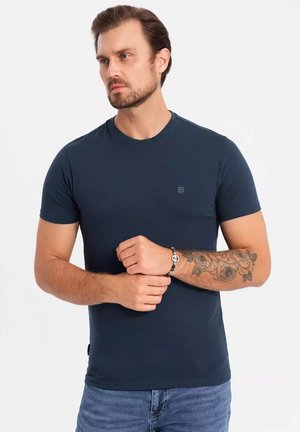 T-shirt blu navy a maniche corte realizzato in tessuto leggero, con scollatura tonda e piccolo logo sul petto. Indossato con jeans in denim.