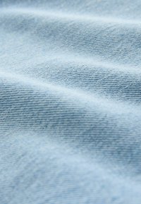 Lyseblåt denimstof med synlig diagonal vævet struktur og bløde folder, der skaber blide skygger.