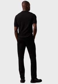 Cămașă polo neagră cu mâneci scurte și pantaloni asortați, amândouă dintr-un material neted. Ținuta are o croială clasică și un design simplu.