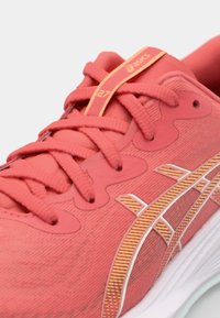 Chaussure de course rouge avec un dessus texturé, fermeture à lacets et accents jaunes. Présente un logo rayé blanc et une semelle rembourrée.