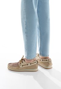 Scarpe casual beige e marroni in suede con un design allacciato, suola in gomma e occhielli decorativi. Indossate con jeans azzurri chiari.
