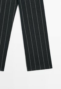Pantalon en denim noir à fines rayures blanches verticales, coupe droite avec ourlet net. Le tissu semble texturé et résistant.