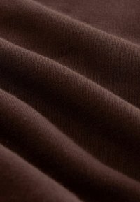 Tissu brun au toucher lisse, présentant un léger rainurage et des plis doux, offrant une apparence douce et uniforme.