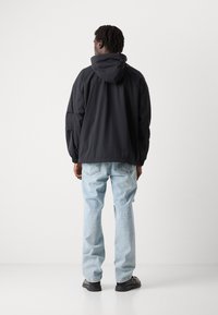 Black hooded jacket with elastic cuffs, loose fit, paired with light blue ripped jeans and black shoes, viewed from the back.