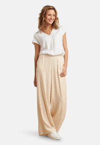 Beige weit geschnittene Hosen mit einem Zickzackmuster, kombiniert mit einem weißen Kurzarmoberteil. Das Outfit zeichnet sich durch eine entspannte Passform und weichen Stoff aus.