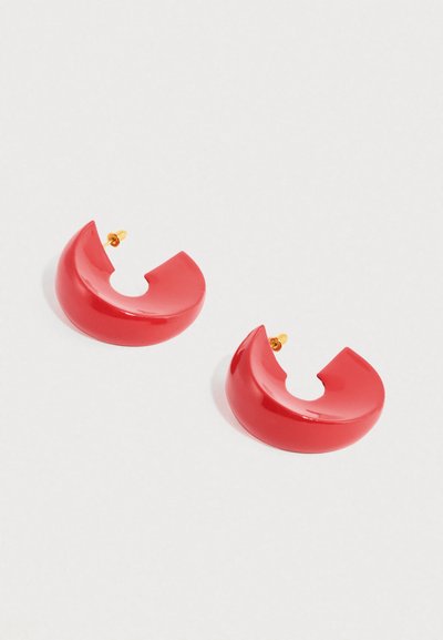Κόκκινα σκουλαρίκια κρίκοι από πολυμερές με γυαλιστερό φινίρισμα, που έχουν ημικυκλικό σχήμα και ανοιχτό τμήμα στο πάνω μέρος, στερεωμένα με καρφί χρώματος χρυσού.