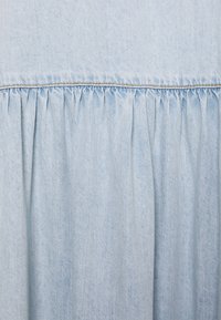 Vaaleansininen farkkukangas, jossa on kerroksellista yksityiskohtaa vyötäröllä. Sileä kangas, jossa on hienovaraisia sävyerotuksia.