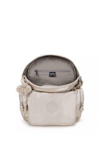 Sac kipling beige clair avec une texture lisse, doté d'un compartiment zippé et d'un accessoire de porte-clés en forme de singe en peluche. L'intérieur possède une poche zippée.