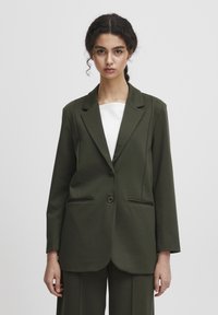 Olivově zelený blazer vyrobený z texturované tkaniny, s klopovým límcem, dvěma předními kapsami a dvouřadým zapínáním. Navržen s volným střihem.
