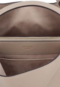 Tan leather shoulder bag interior with a zippered pocket, smooth texture, and gold hardware. Brand name embossed on a leather patch.