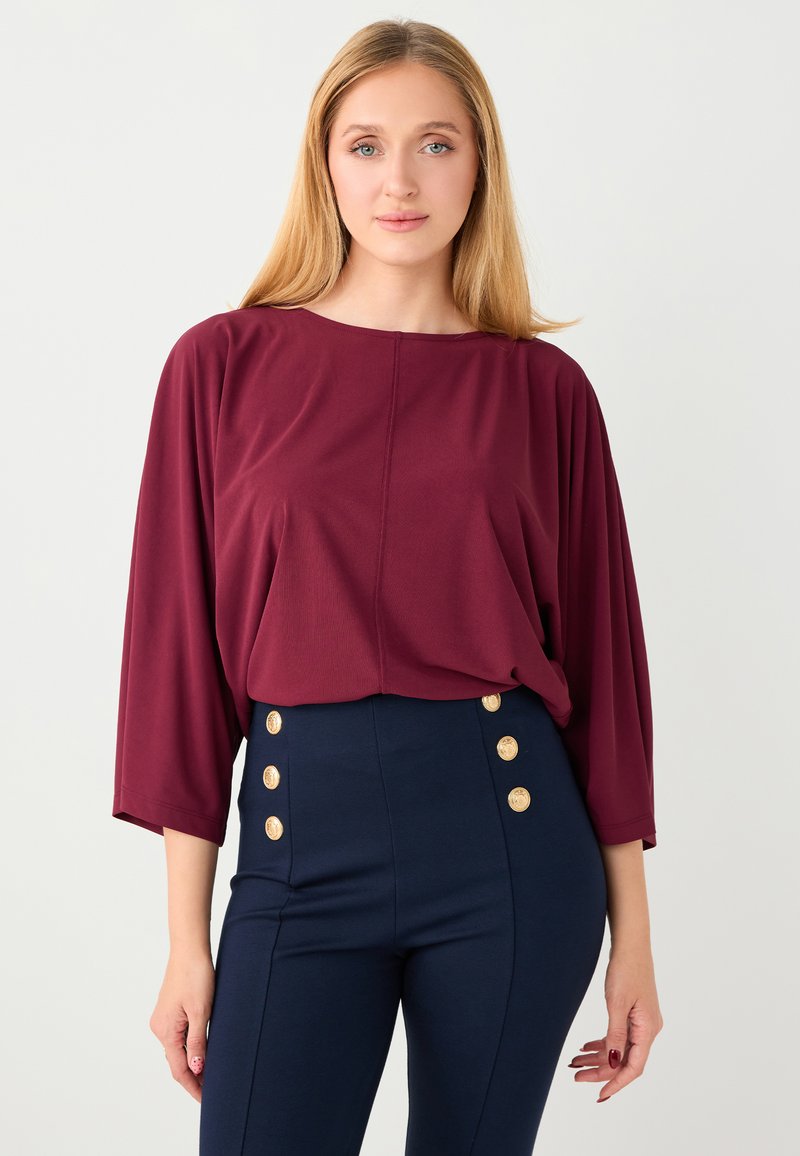 Haut en tissu doux bordeaux avec un col bateau et des manches trois-quarts, associé à un pantalon taille haute bleu marine avec des boutons dorés.