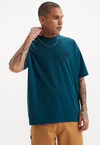 Tricou din bumbac de culoare teal, cu mâneci scurte și decolteu tip crew, având un logo Levi's negru pe piept și o croială lejeră.