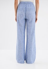 Blauwe en witte gestreepte wijde broek van lichtgewicht stof met een elastische tailleband en verticale lijnen in verschillende breedtes.