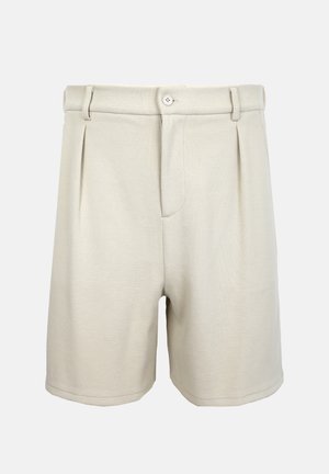 Béžové šortky na míru s předním zapínáním na knoflík a zip, poutky na pásek a jemnými předními sklady na jednobarevném pozadí.