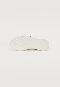 Semelle d'une chaussure, en caoutchouc blanc avec des stries et des motifs pour la traction ; conçue avec une surface lisse, plate et une légère courbure.