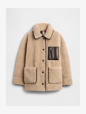 Casaco sherpa bege com um bolso com fecho em pele castanha, grandes bolsos frontais e gola, apresentando acabamentos e botões escuros em contraste.