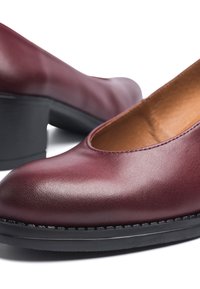 Zapato de charol burdeos con puntera redondeada, suela negra y detalles de costura. Textura suave y tacón moderado, diseñado para mayor comodidad al usar.