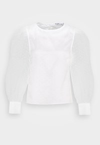 Blouse blanche avec motif à points texturés, manches bouffantes transparentes, encolure ronde et poignets blancs unis. Ouverture dos en trou de serrure, tissu lisse.