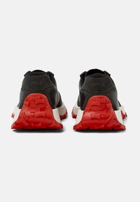 Scarpe da ginnastica nere con tomaia texture, dotate di una suola in gomma rossa audace. Dettagliate con un arco leggero e tallone imbottito per il supporto.