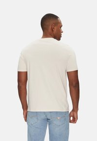 Camiseta corta de manga corta en color crema, confeccionada en una tela suave y ligera. La vista desde la parte de atrás muestra un escote redondo y una textura lisa, combinada con jeans de denim claros.