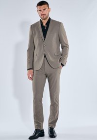 Beige suit made of smooth fabric, single-breasted jacket with a pocket, paired with black shirt and sleek black shoes. Tailored fit.