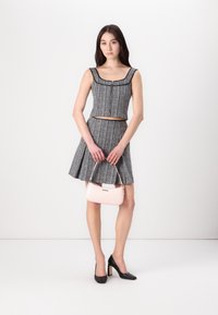 Top court en tweed noir et blanc avec décolleté carré, associé à une jupe évasée. Tient un petit sac à main rose. Chaussures à talons hauts noires.