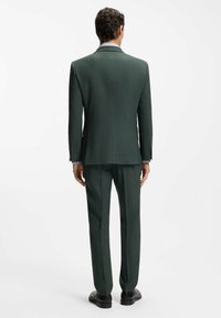 Dunkelgrüner Anzug mit maßgeschneidertem Sakko und gerade geschnittenen Hosen, gefertigt aus strukturiertem Stoff mit klassischer Passform und dezenten Details.