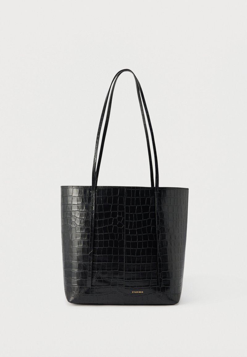 Μαύρη τσάντα ώμου με υφή κροκόδειλου και μακριές λαβές, όρθια σε απλό φωτεινό φόντο.