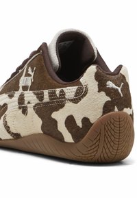 Ténis de camurça castanho e bege com um padrão de camuflagem, apresentando uma sola de borracha texturizada e o logo da Puma no calcanhar e na lateral.