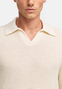 Maglione lavorato a maglia in off-white con un motivo strutturato a nido d'ape, caratterizzato da un colletto morbido bicolore e un design a V.