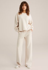 Pullover beige con collo rotondo e spalle scese abbinato a pantaloni beige a gamba larga. Tessuto morbido con una texture liscia, design minimale.