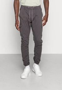 Grijs cargobroek met een elastische tailleband en trekkoord, voorzien van zijzakken en aangesloten boorden, gestyled met witte sneakers.