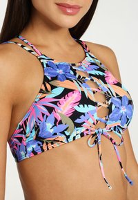 Top de bikini floral con patrones multicolores sobre un fondo negro, con un diseño de cuello halter y detalles de corte en la parte frontal.